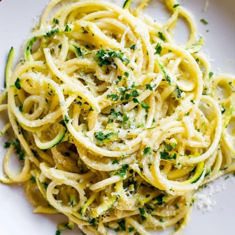 Freshly cooked Lemon Zucchini Pasta with spiralized zucchini and grated Parmesan on a white plate, garnished with parsley.  