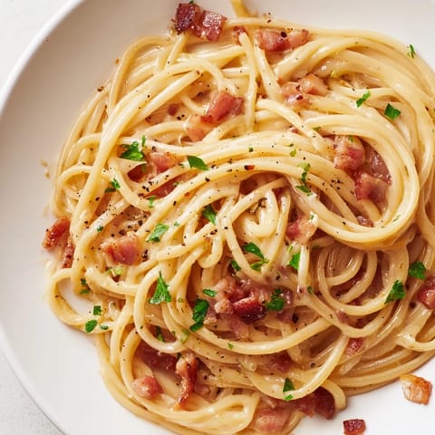 Steaming bowl of homemade crispy bacon linguine, garnished with fresh parsley and a sprinkle of Parmesan, ready to serve.  