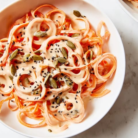 Colorful vegan Carrot Noodle Skincare Bowl featuring fresh spinach, red bell peppers, and a drizzle of tahini-lime dressing.