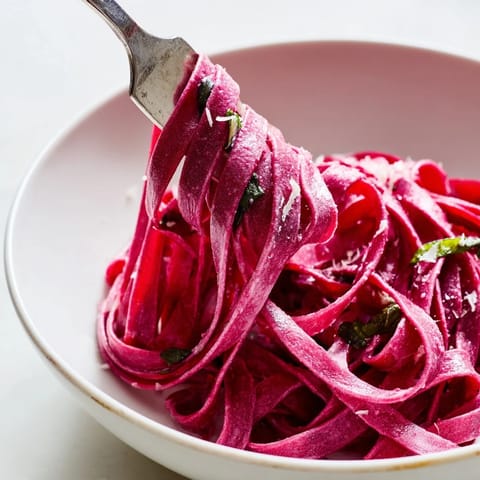 A close-up view of homemade beet noodle pasta arranged in a nest, showcasing the rich pink color and texture.  
