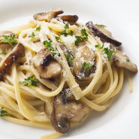 A rustic skillet of creamy mushroom linguine rests beside a glass of white wine, showcasing savory mushrooms in light cream.