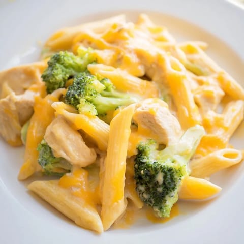 A close-up of steaming Chicken Broccoli Cheddar Pasta, featuring tender chicken pieces, bright broccoli, and a velvety cheddar sauce ready to serve.
