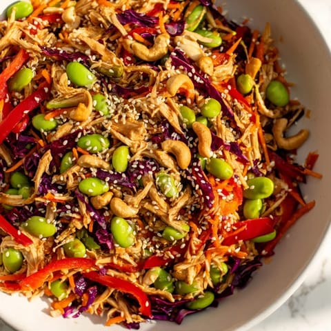 Close-up of Edamame Crunch Chicken Salad topped with toasted sesame seeds and chopped cashews, served in a rustic white bowl.