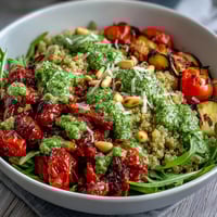 Vibrant bowl of quinoa and roasted vegetables tossed in homemade arugula pesto, garnished with Parmesan.